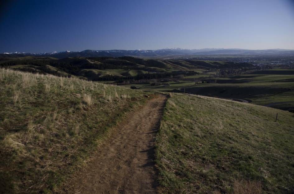 Trail heading down grassy hillside with valley and mountain views