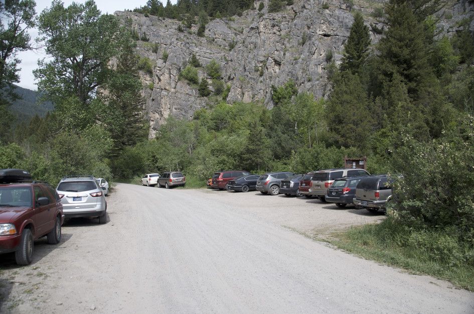 Gravel trailhead parking area with cars beneath dramatic limestone cliffs
