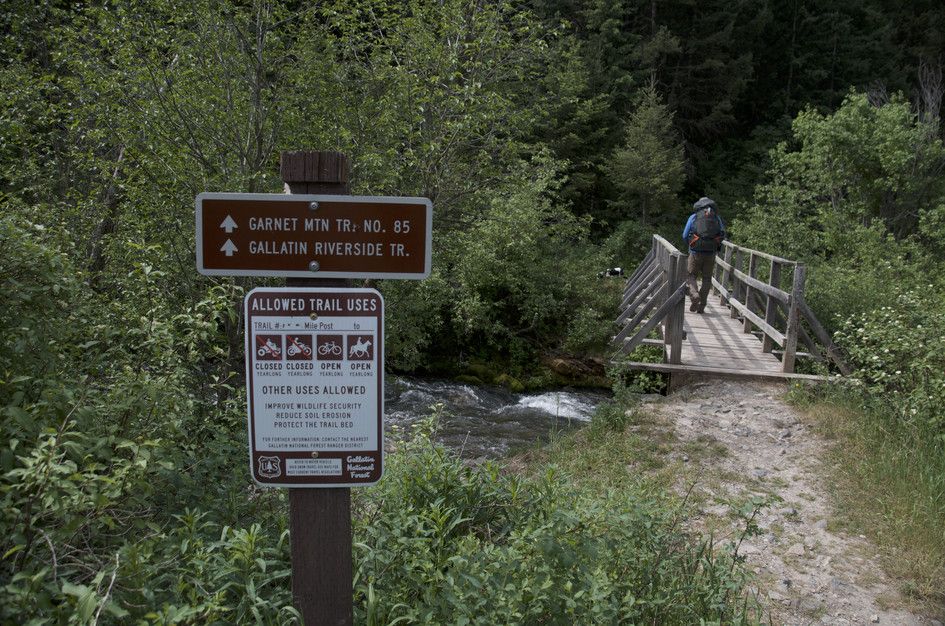 Trail sign for Garnet Mountain Trail and Gallatin Riverside Trail with wooden bridge