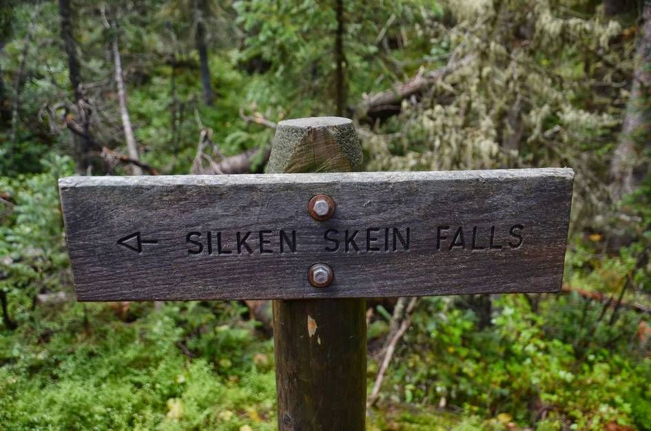 Weathered wooden trail sign for Silken Skein Falls in lush forest