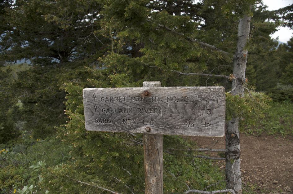 Weathered wooden trail sign showing directions to Garnet Mountain and Gallatin River