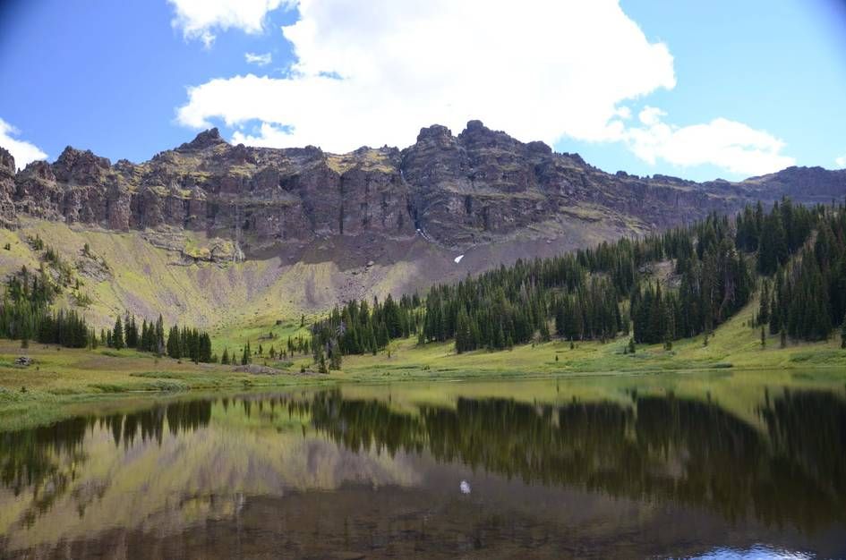 Hyalite Lake reflecting rocky cirque cliffs with spruce forest and green meadow