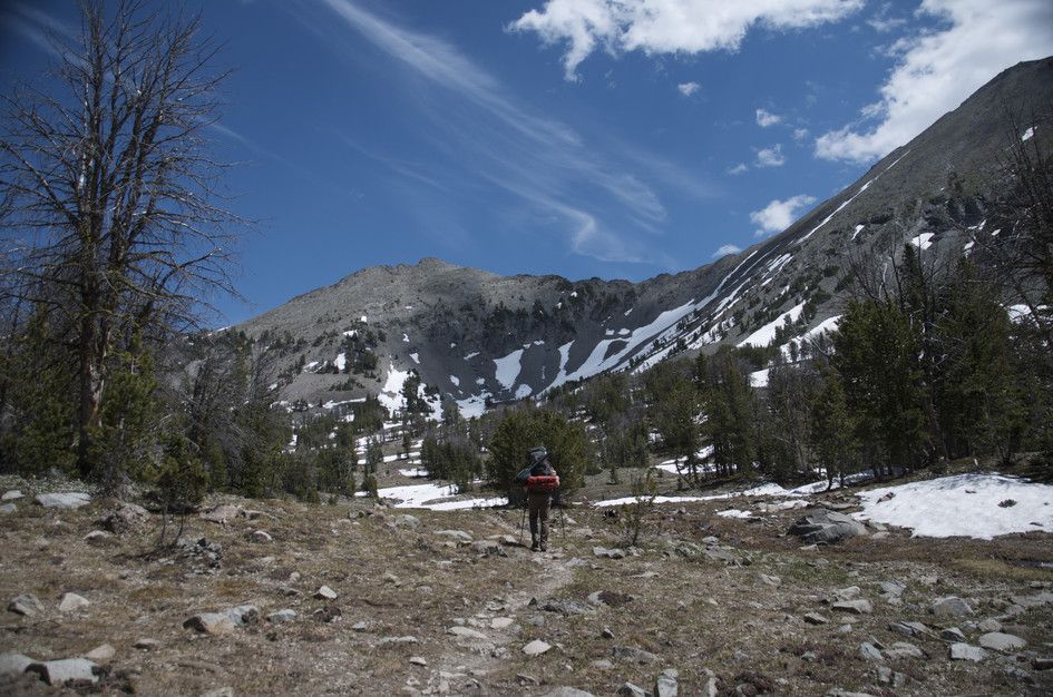 Backpacker approaching snowfield with snow-covered alpine cirque ahead
