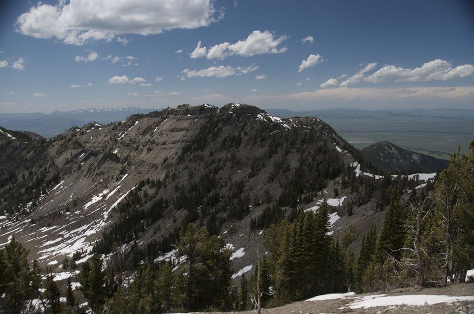 Ridge view of forested peak with snow patches and prairie valley beyond