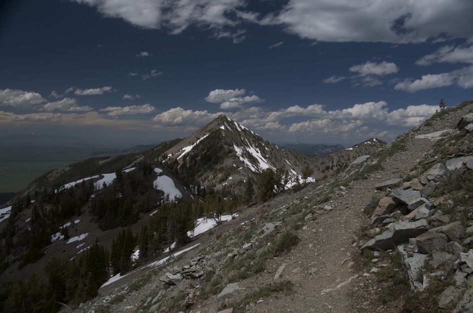 Rocky ridge trail with dramatic snow-covered peak and green valley below