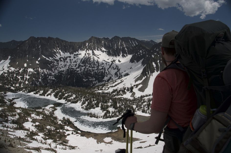 Backpacker with trekking poles overlooking frozen Campfire Lake and snow-covered cirque