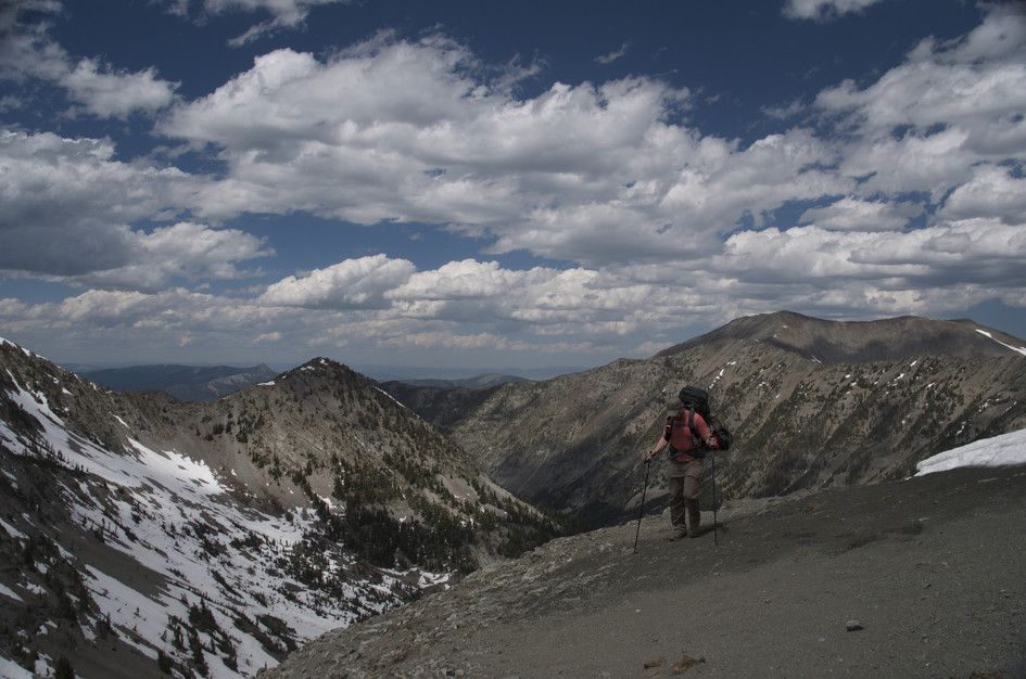 Backpacker standing on ridge overlooking deep forested valley and peaks