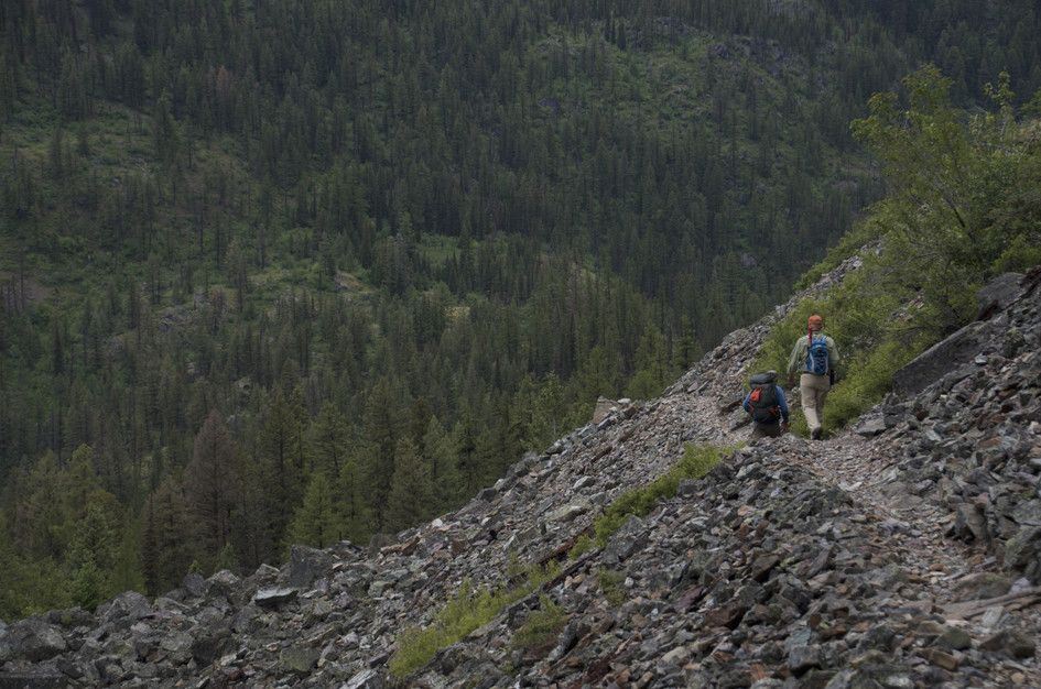 Hikers traversing rocky scree slope with forested valley below