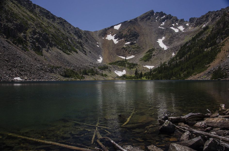 Deep alpine lake in rocky cirque with snow patches and driftwood