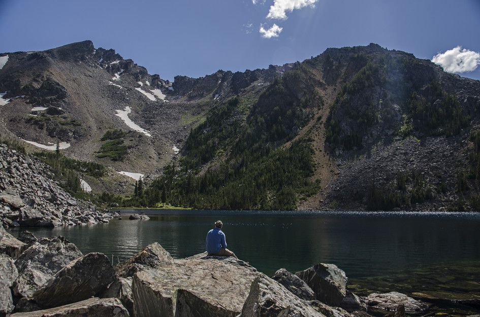 Person sitting on boulder overlooking turquoise lake and rugged cirque