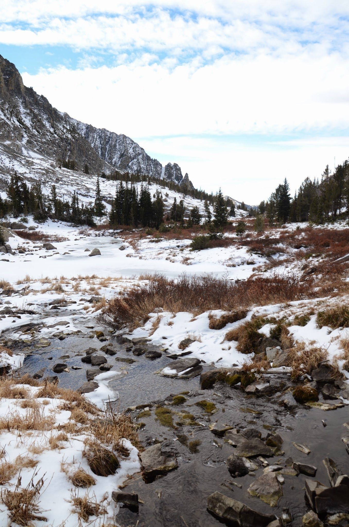 Mountain stream flowing through snowy basin toward jagged peaks