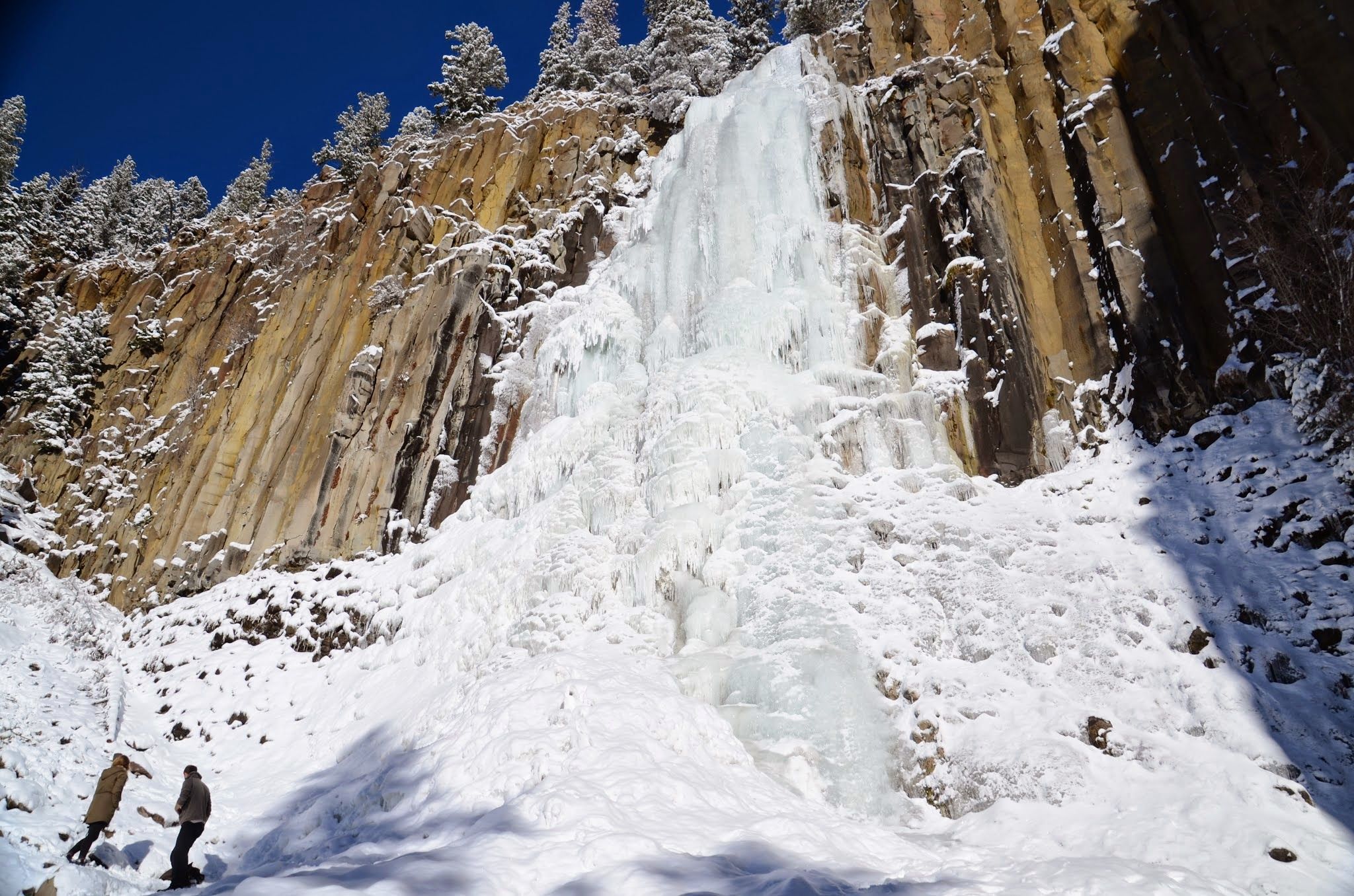 Person standing at the base of frozen Palisade Falls showing the massive scale of the ice