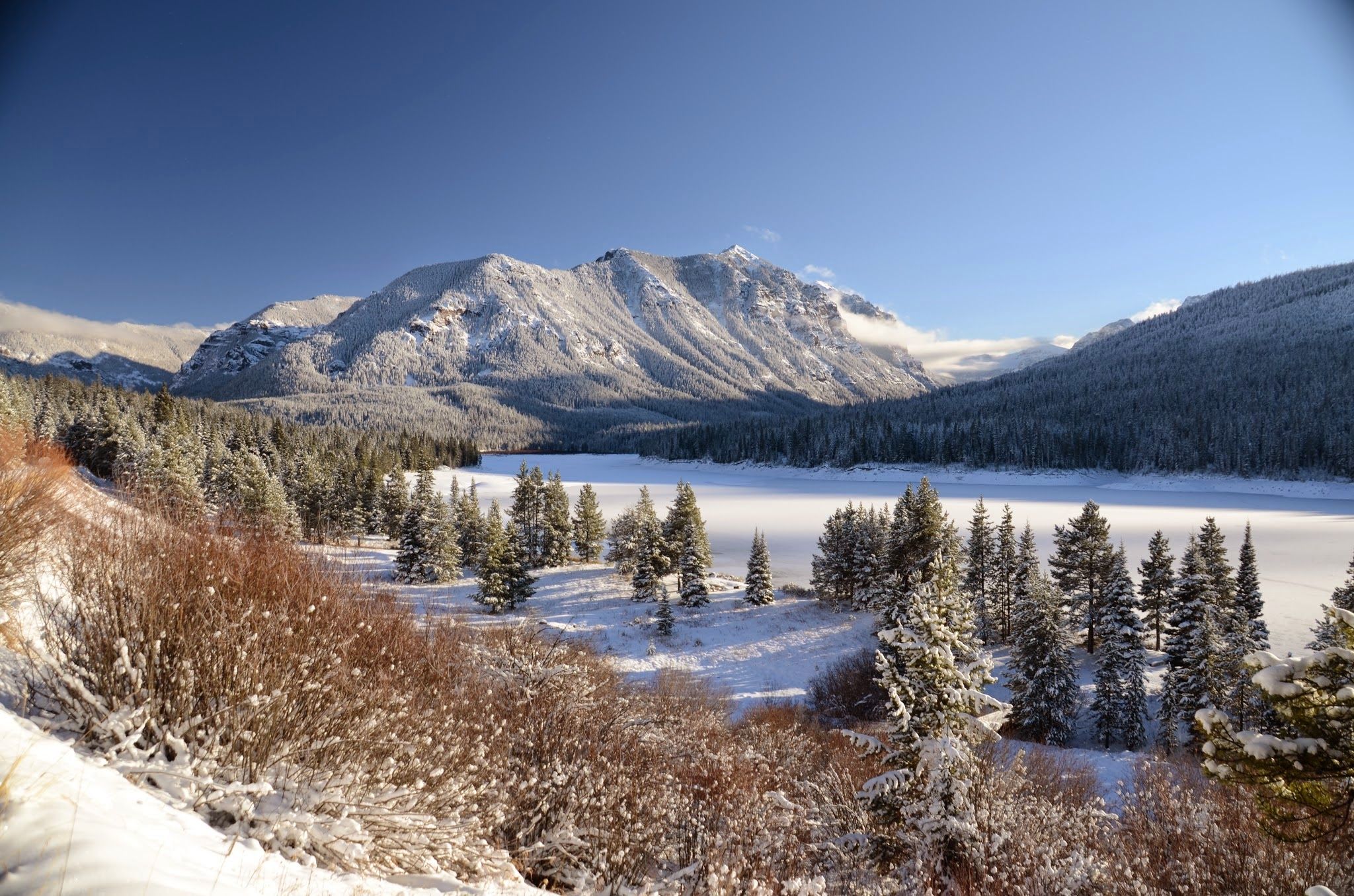 Hyalite Reservoir in winter with snow-covered mountains and frosted evergreen trees
