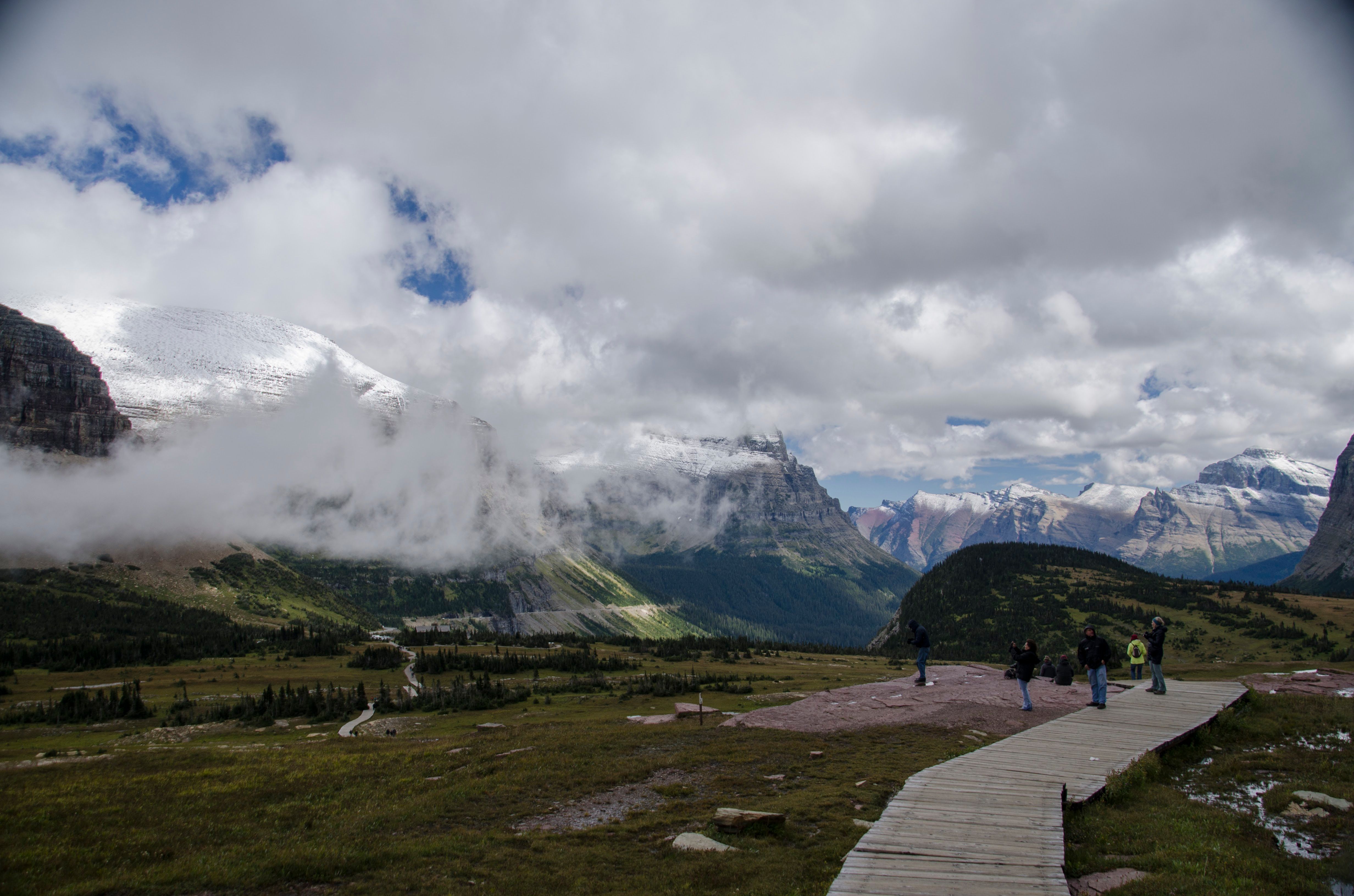 Boardwalk through alpine meadow with hikers looking back toward snow-capped peaks