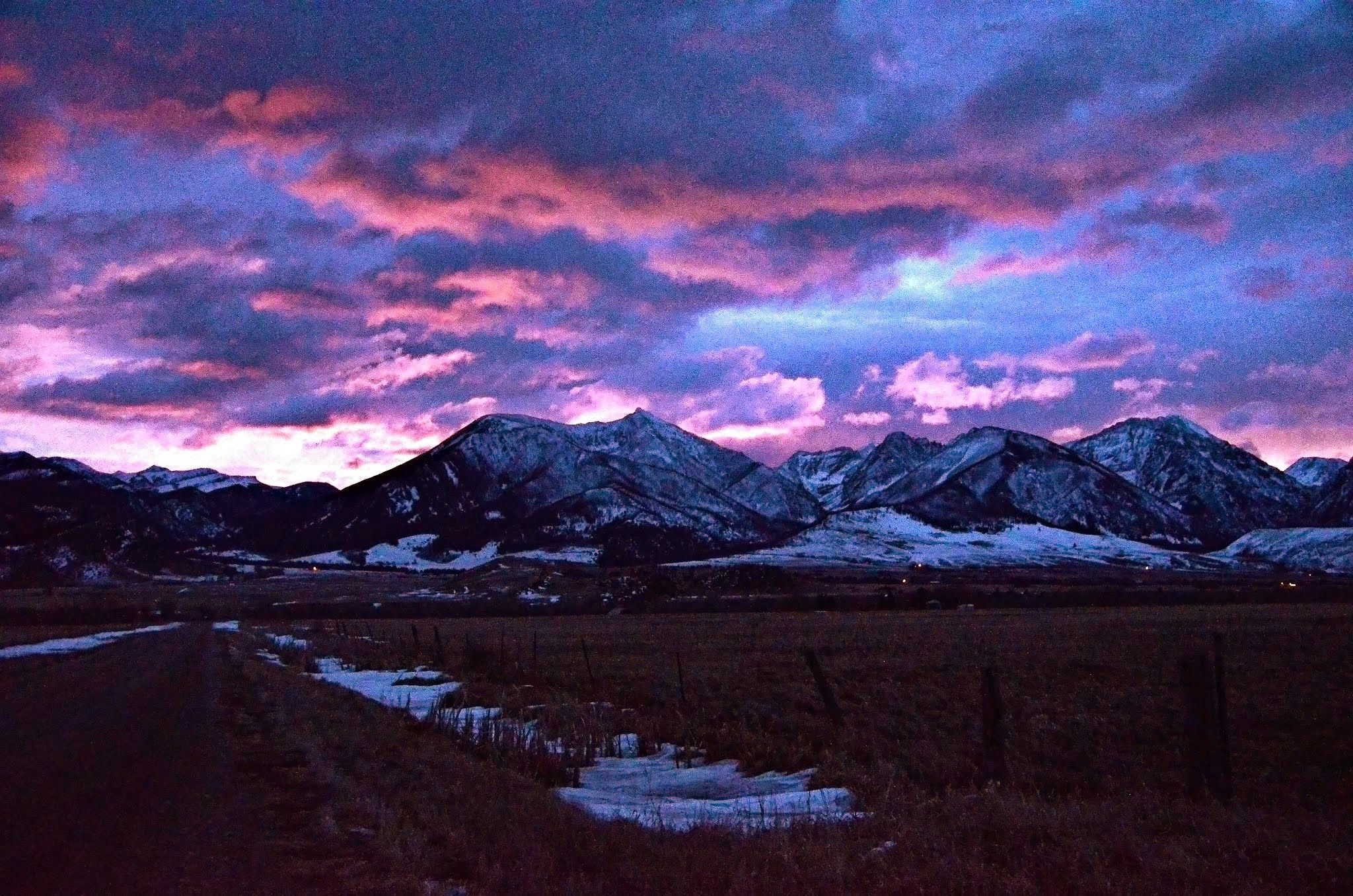 Pre-dawn sky over Yellowstone with deep purple and pink clouds above snow-capped mountains and a dark empty road