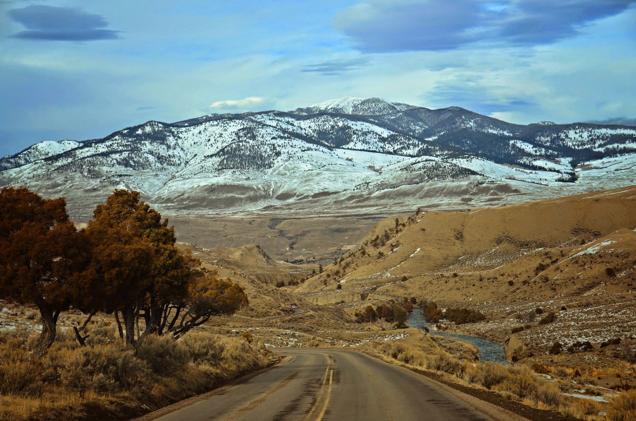 Two-lane road descending toward the Yellowstone valley with golden brush and mountains on the horizon