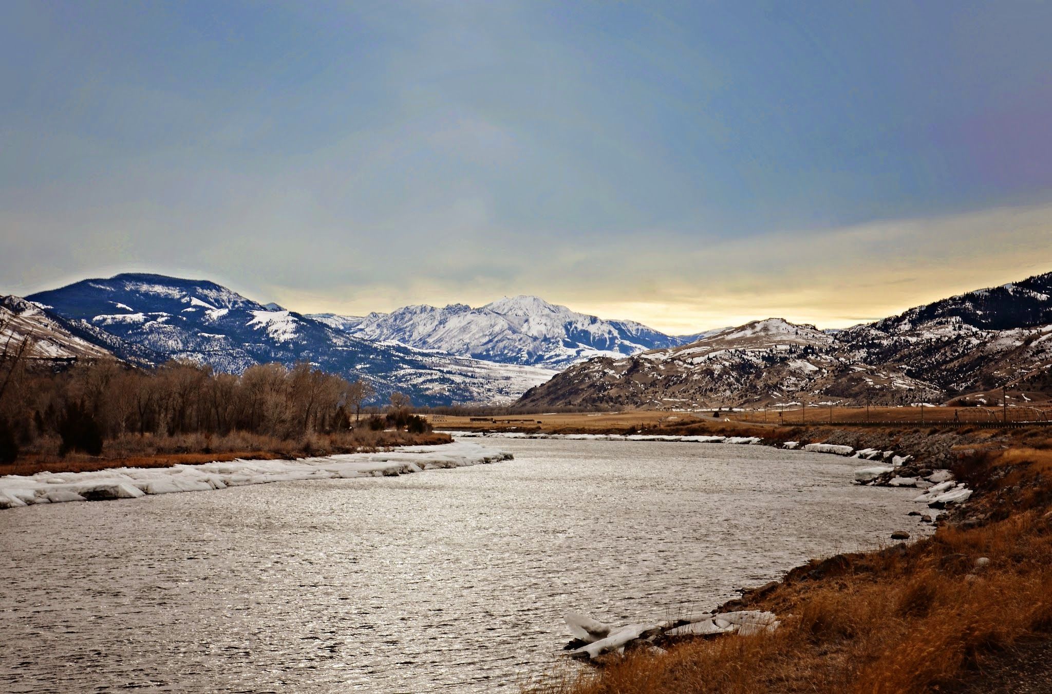 The Yellowstone River winding through an empty winter valley with snow-covered peaks and bare cottonwood banks