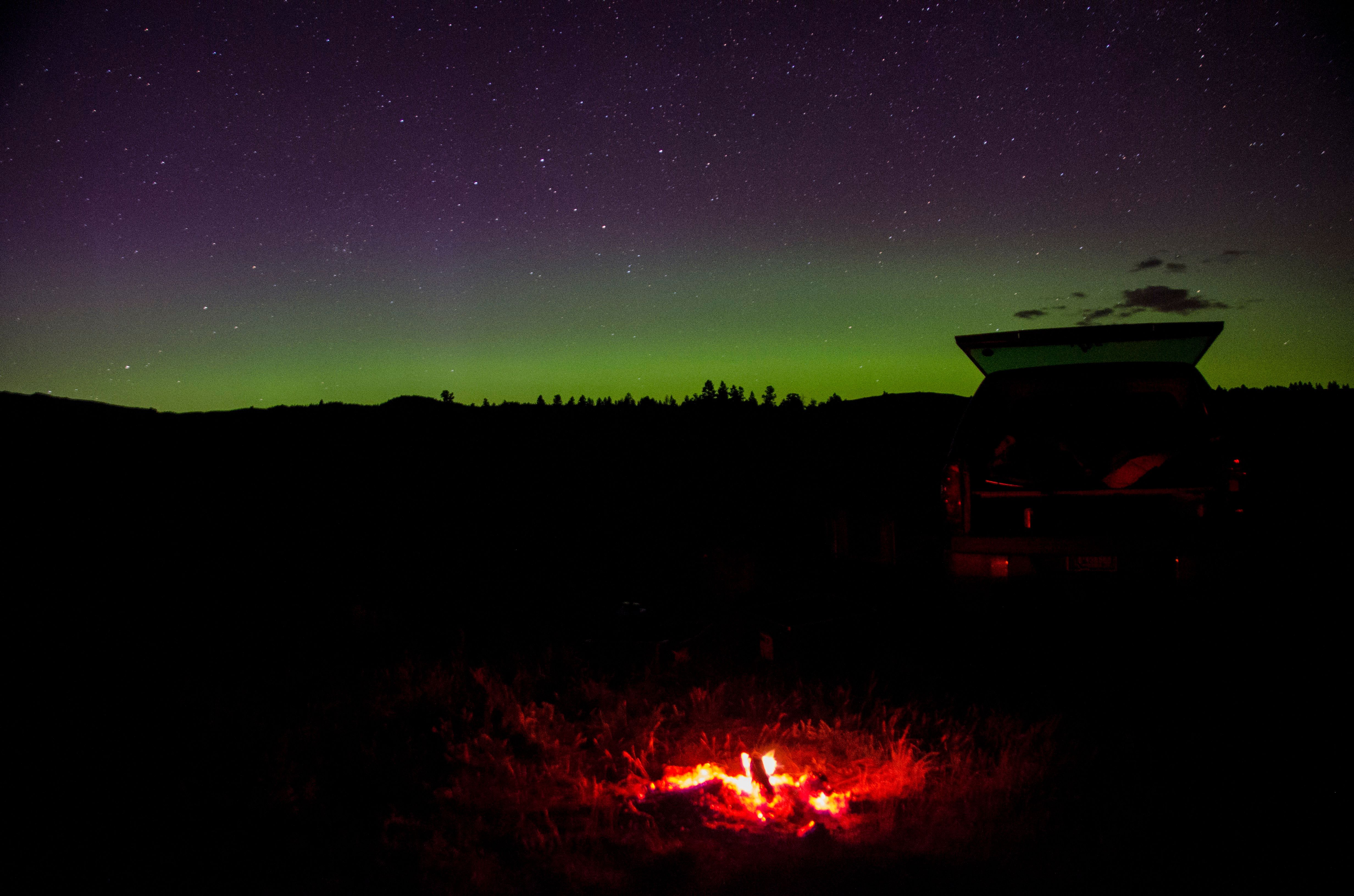 Campfire and truck under the northern lights at a dispersed campsite in Montana