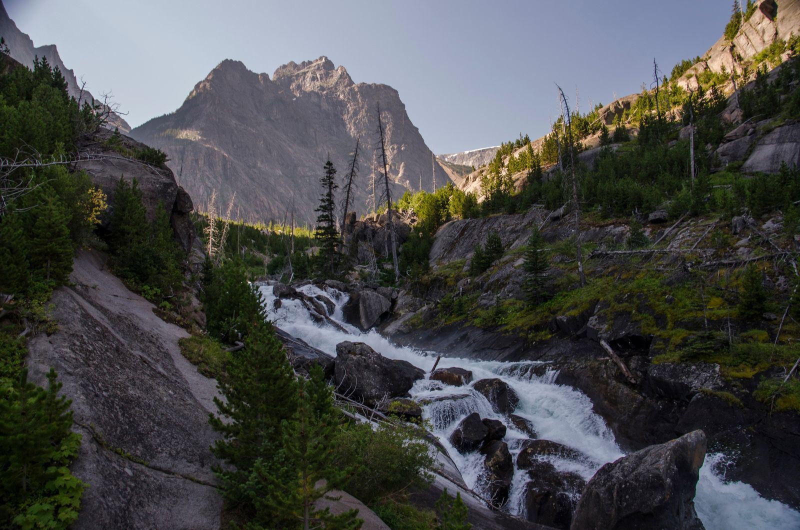 Rushing creek cascading over boulders with jagged Beartooth peak behind