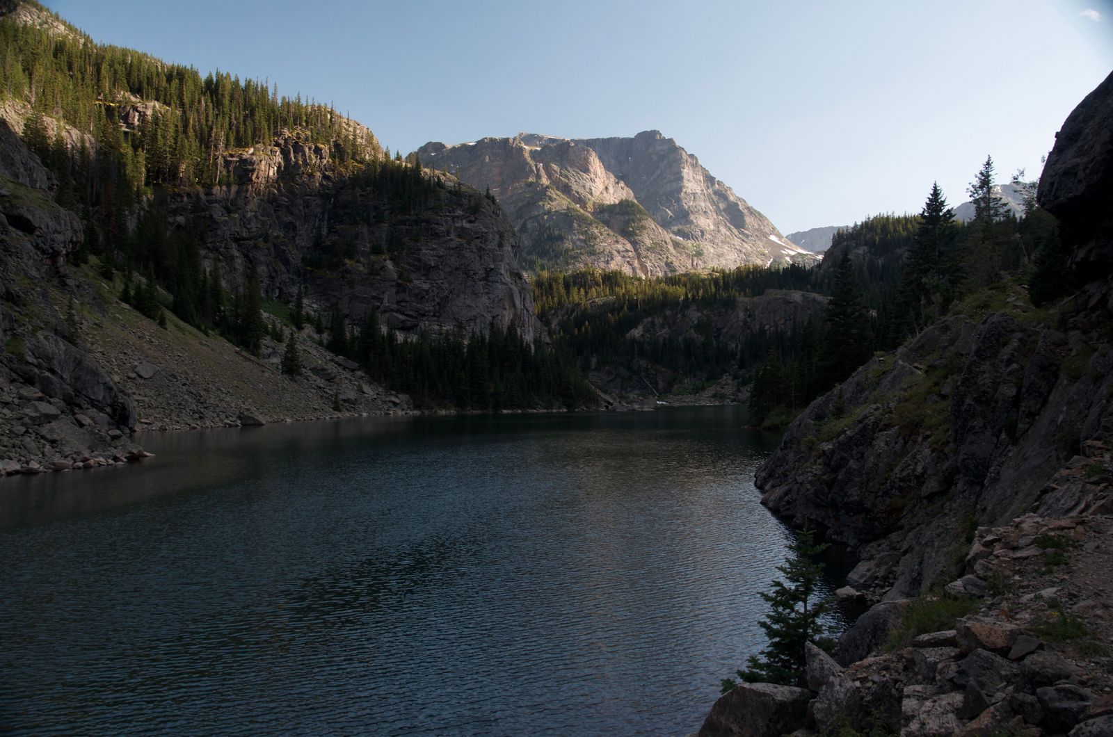 Alpine lake reflecting massive granite peak with steep cliffs and sparse forest