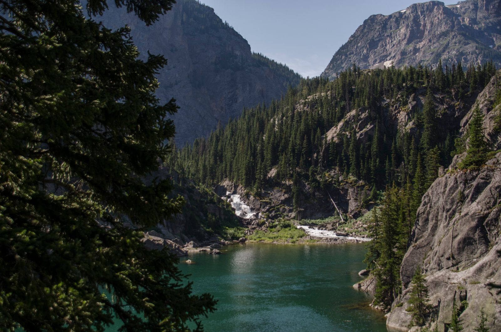 Turquoise alpine lake with waterfall and steep forested granite walls