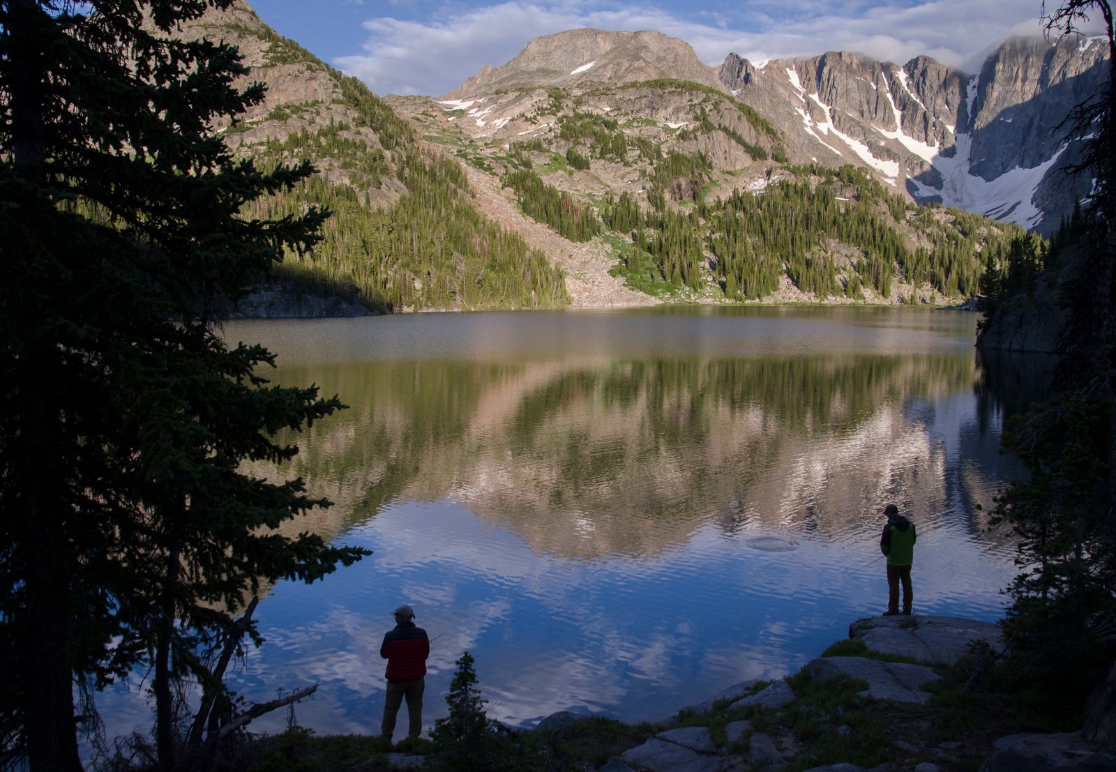 Two backpackers viewing lake with mirror reflection of granite peaks at sunrise