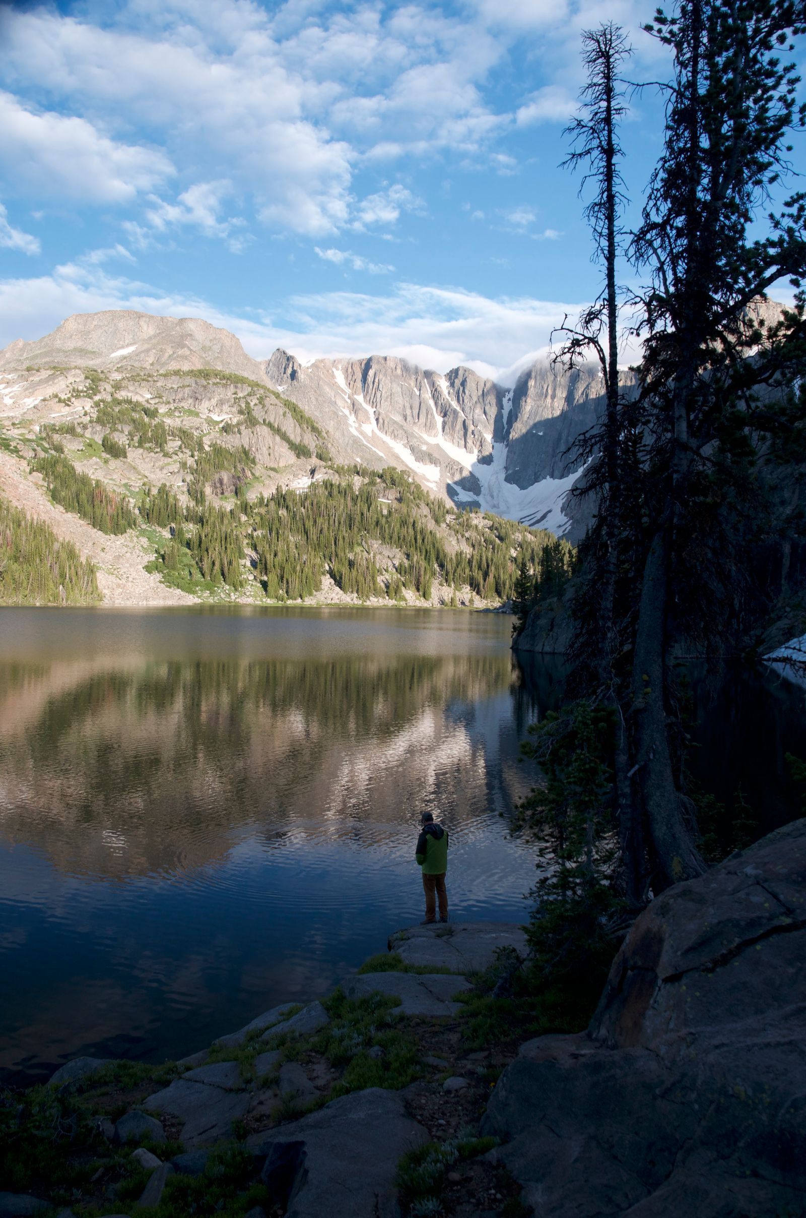 Backpacker standing at lake shore with dramatic granite cirque and glaciers