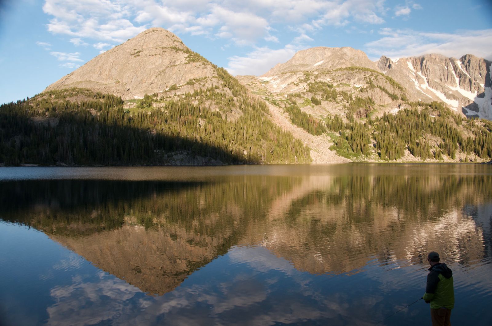 Pyramid-shaped peak reflected in calm alpine lake with angler fishing