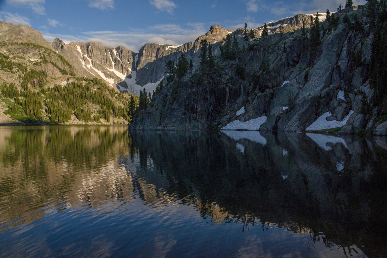 Pristine alpine lake reflecting granite cliffs and scattered evergreens
