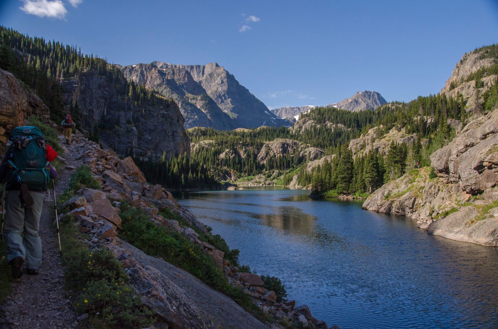 Backpackers hiking rocky trail alongside deep blue alpine lake