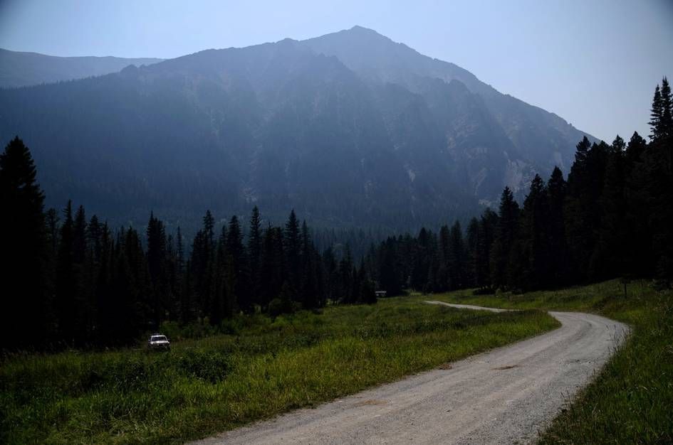 Winding gravel road through meadow with parked vehicle and hazy mountain backdrop