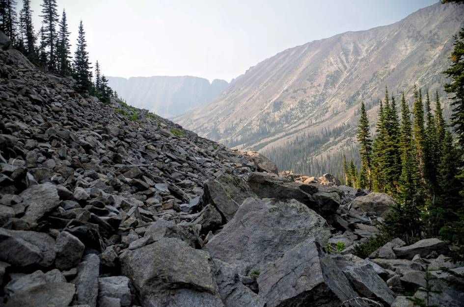 Large boulder field with scattered pines and steep mountain slopes in background