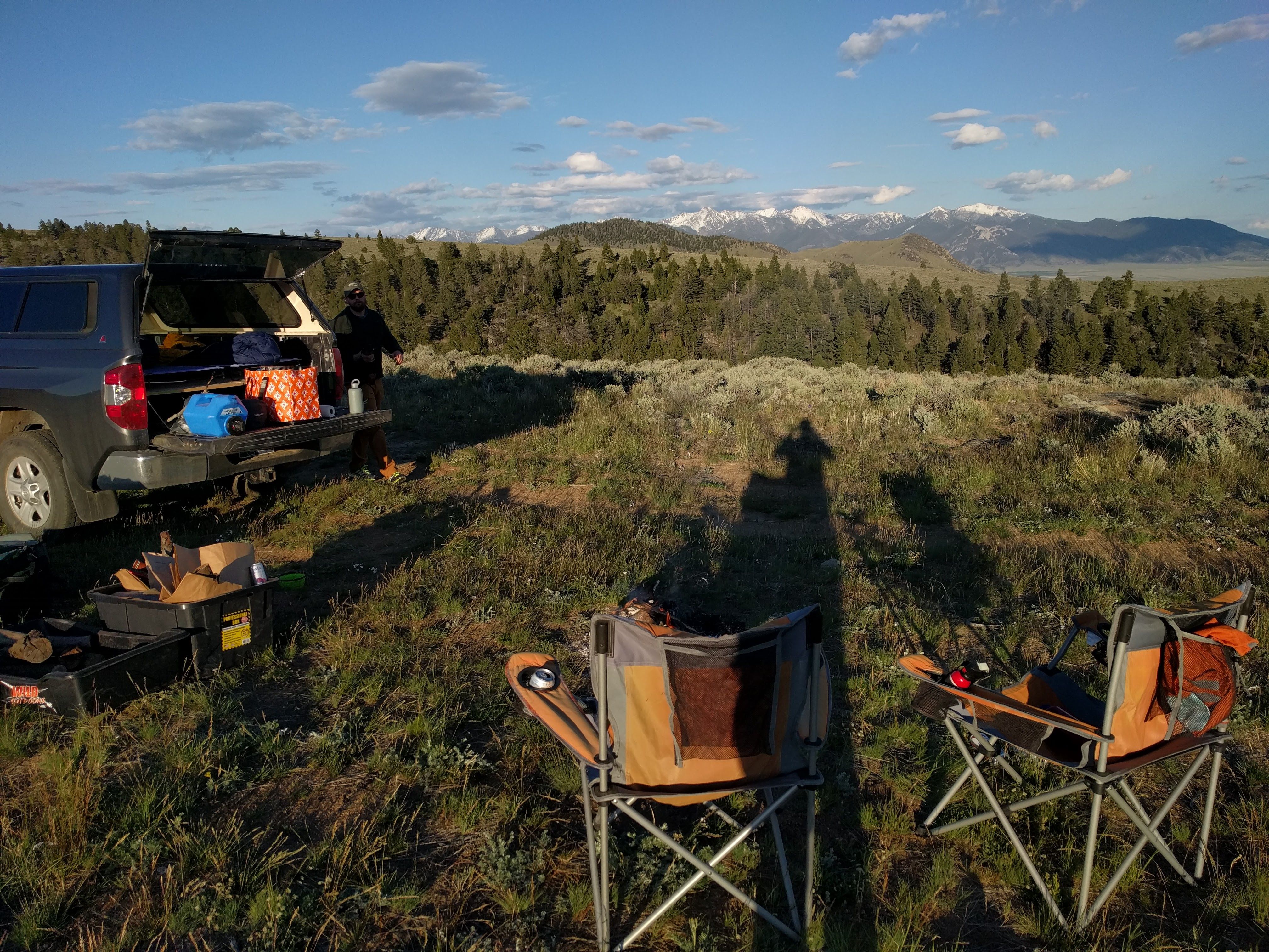 Truck and camp chairs at a dispersed campsite in a sage meadow with snow-capped mountains in the distance