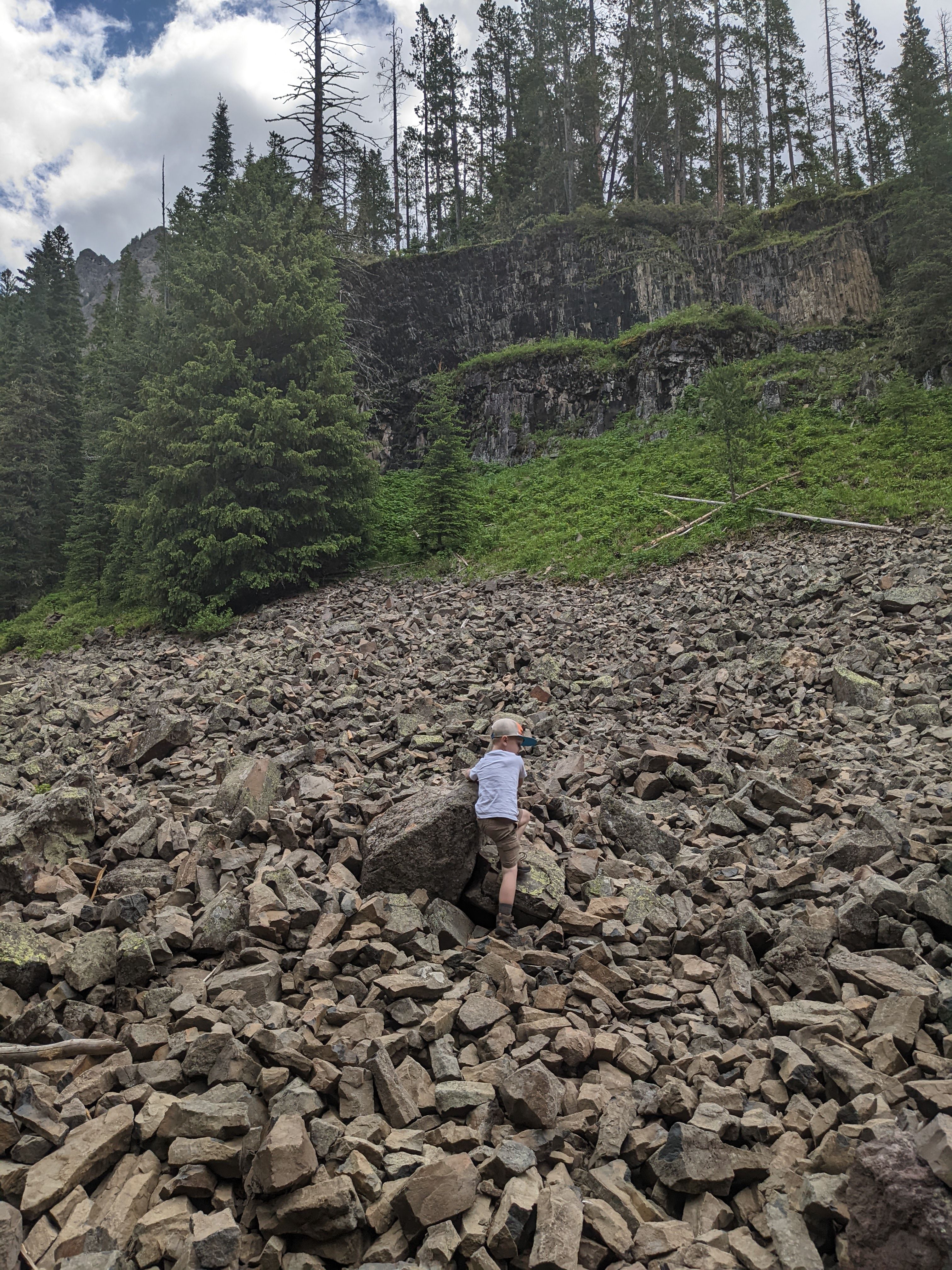 Young child climbing a large talus field below a cliff wall near Grotto Falls