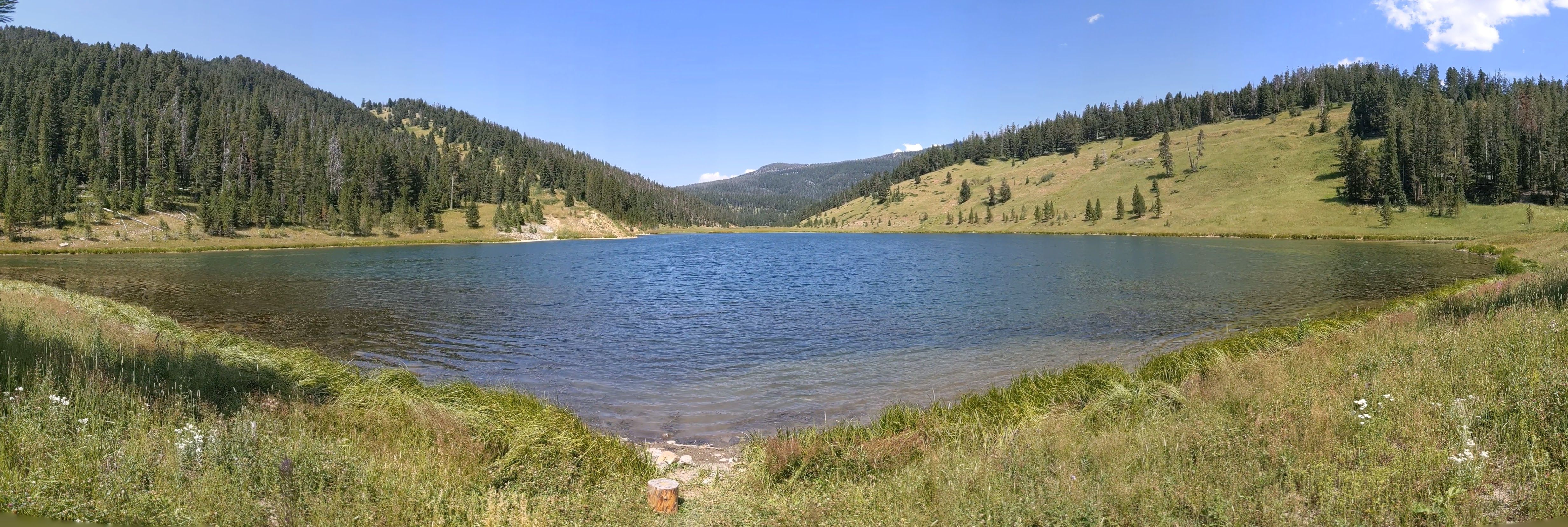 Panoramic view of Mystic Lake surrounded by forested hills and grassy shoreline