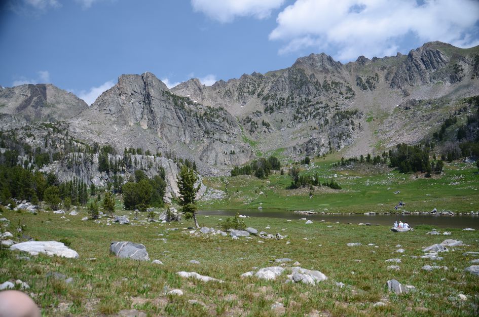 Beehive Basin lake with meadow and visitors beneath towering granite cirque