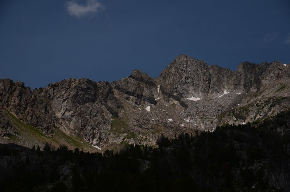 Jagged granite ridge with snow patches against deep blue sky above silhouetted forest