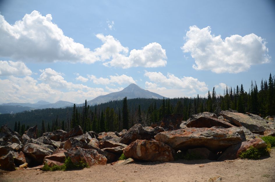 Lone Peak behind rusty orange boulder pile with evergreen forest and blue sky