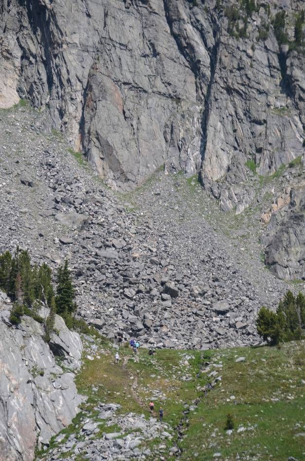 Tiny hikers dwarfed by massive granite cliff face with talus field below