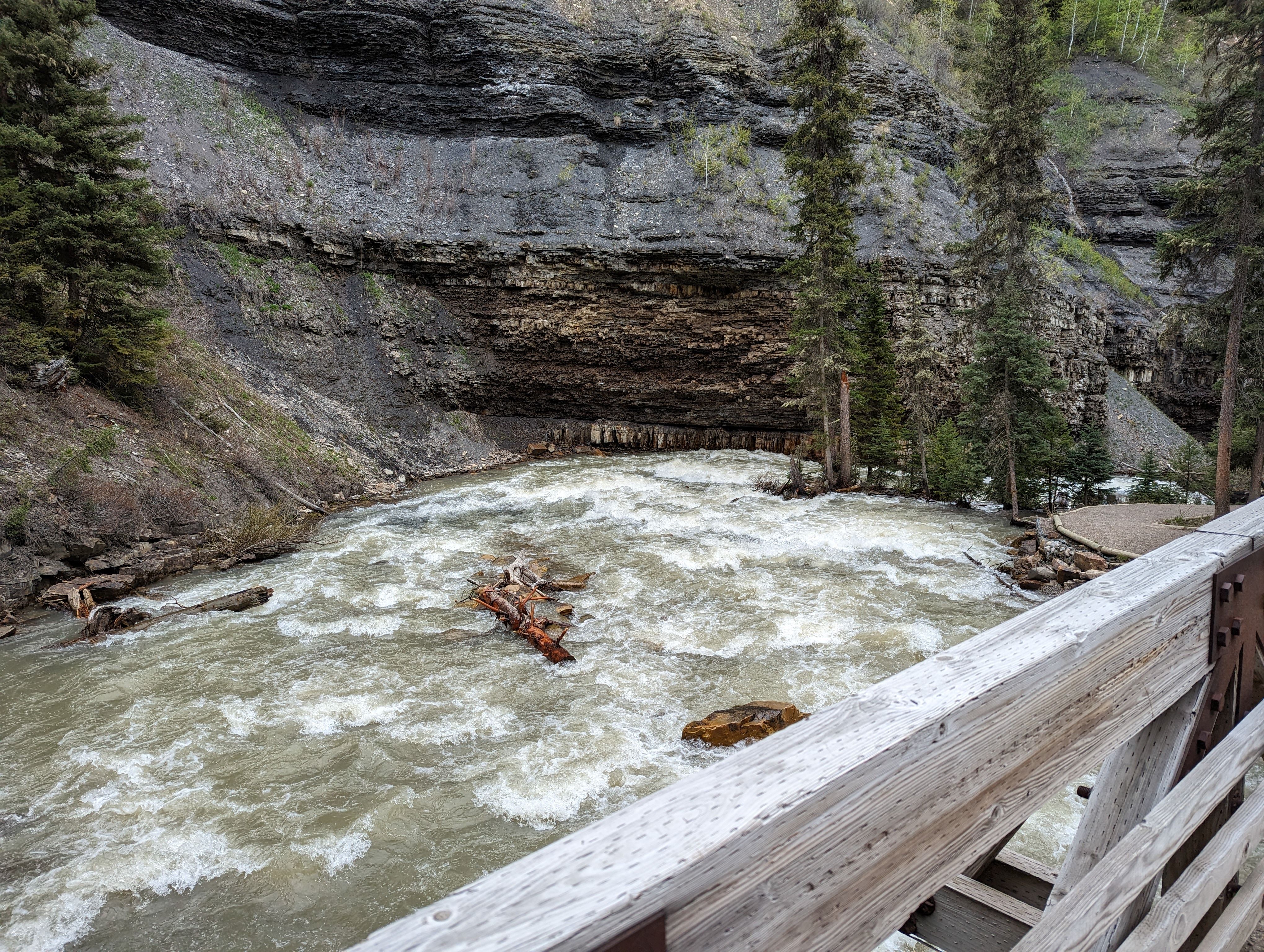 View of rushing whitewater rapids from footbridge with layered rock walls