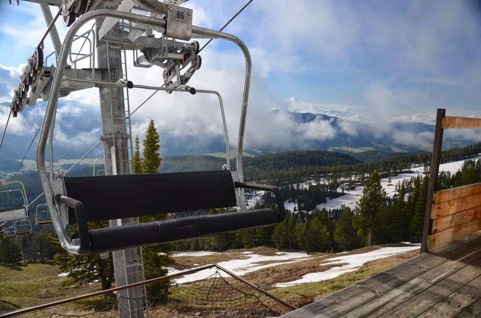 Top of chairlift station with snow patches and distant valley views