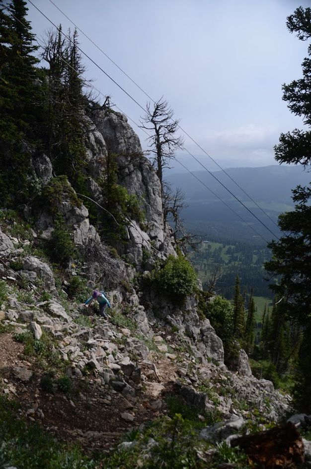 Hiker climbing steep rocky trail beneath massive limestone cliff face