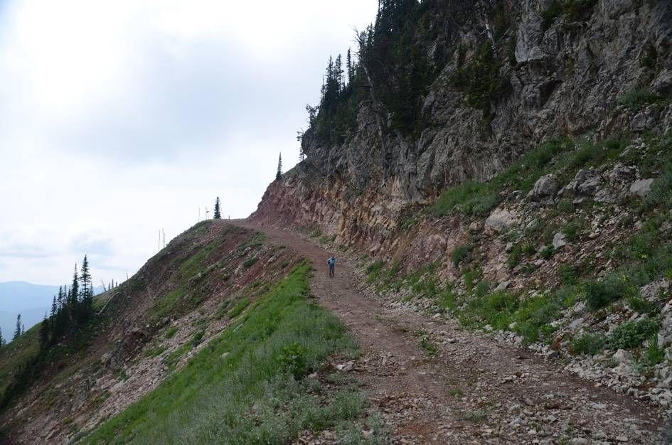 Hiker on service road carved into exposed colorful rock layers on ridge
