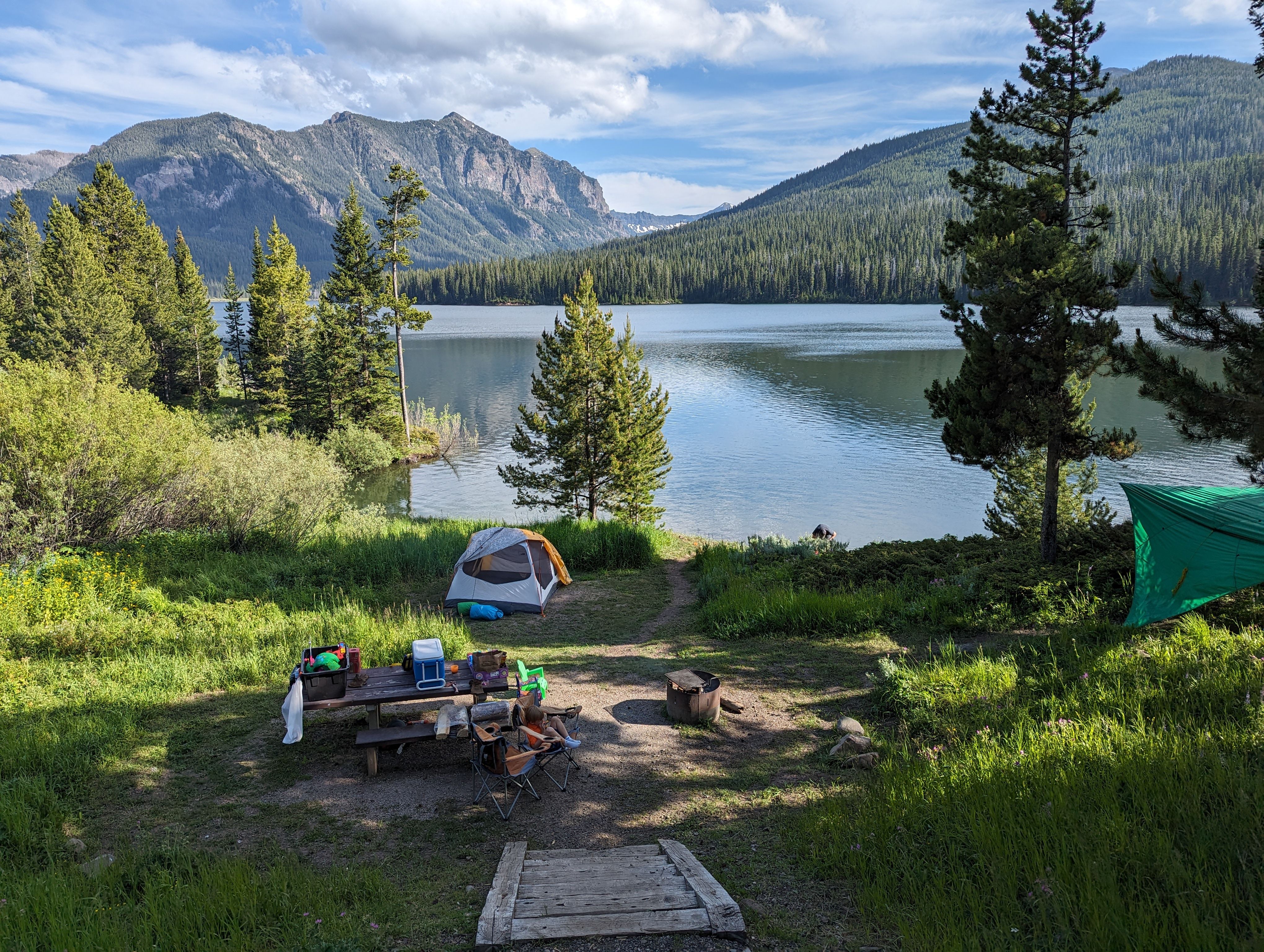 Lakeside campsite with tent and picnic table, dramatic mountains and blue sky reflected in calm water