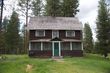 The Old Condon Ranger Station, a two-story dark log cabin with green door surrounded by tall pines