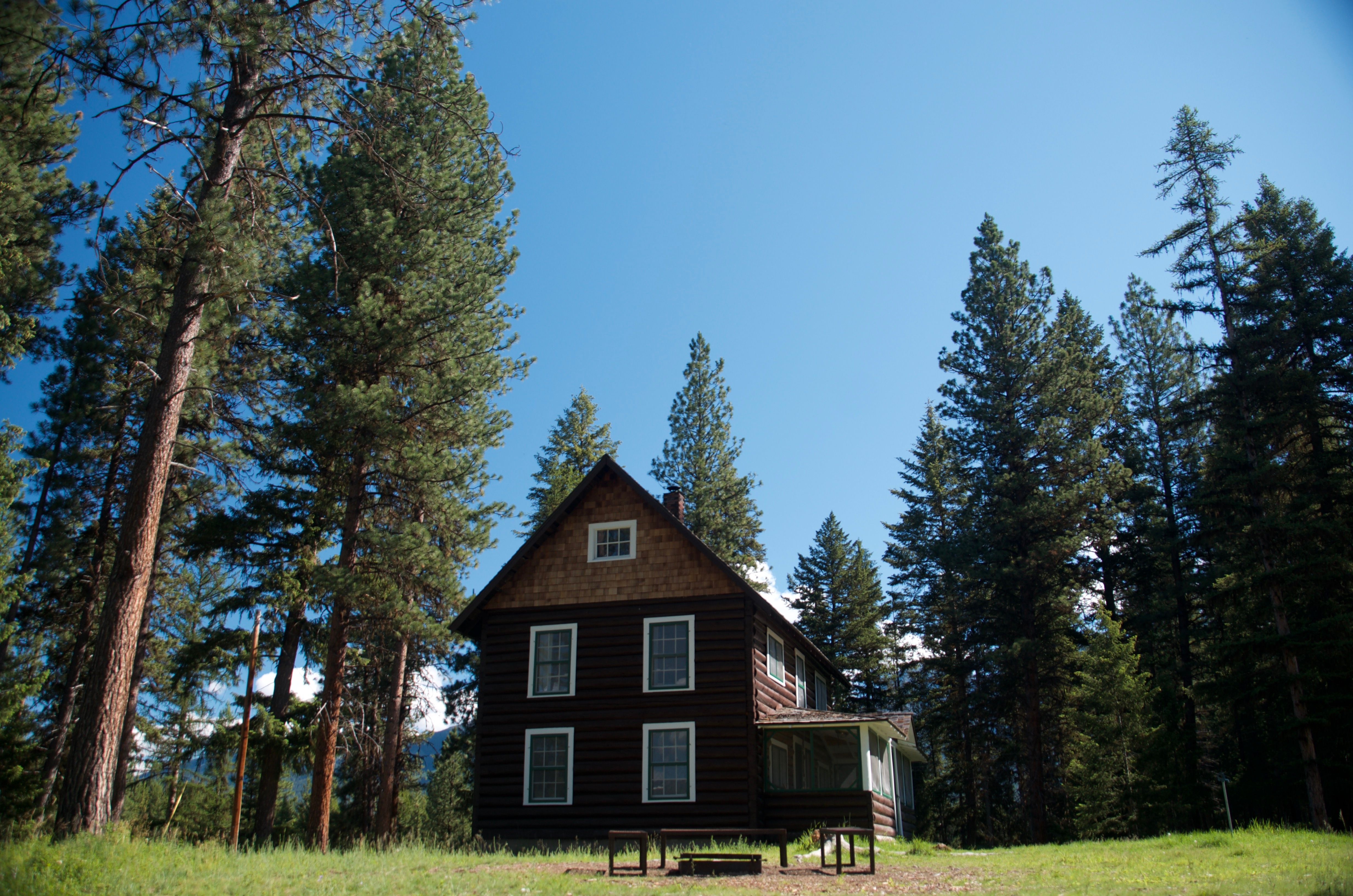 Side view of the Old Condon Ranger Station with dramatic pine trees and snow-capped mountains visible behind the cabin
