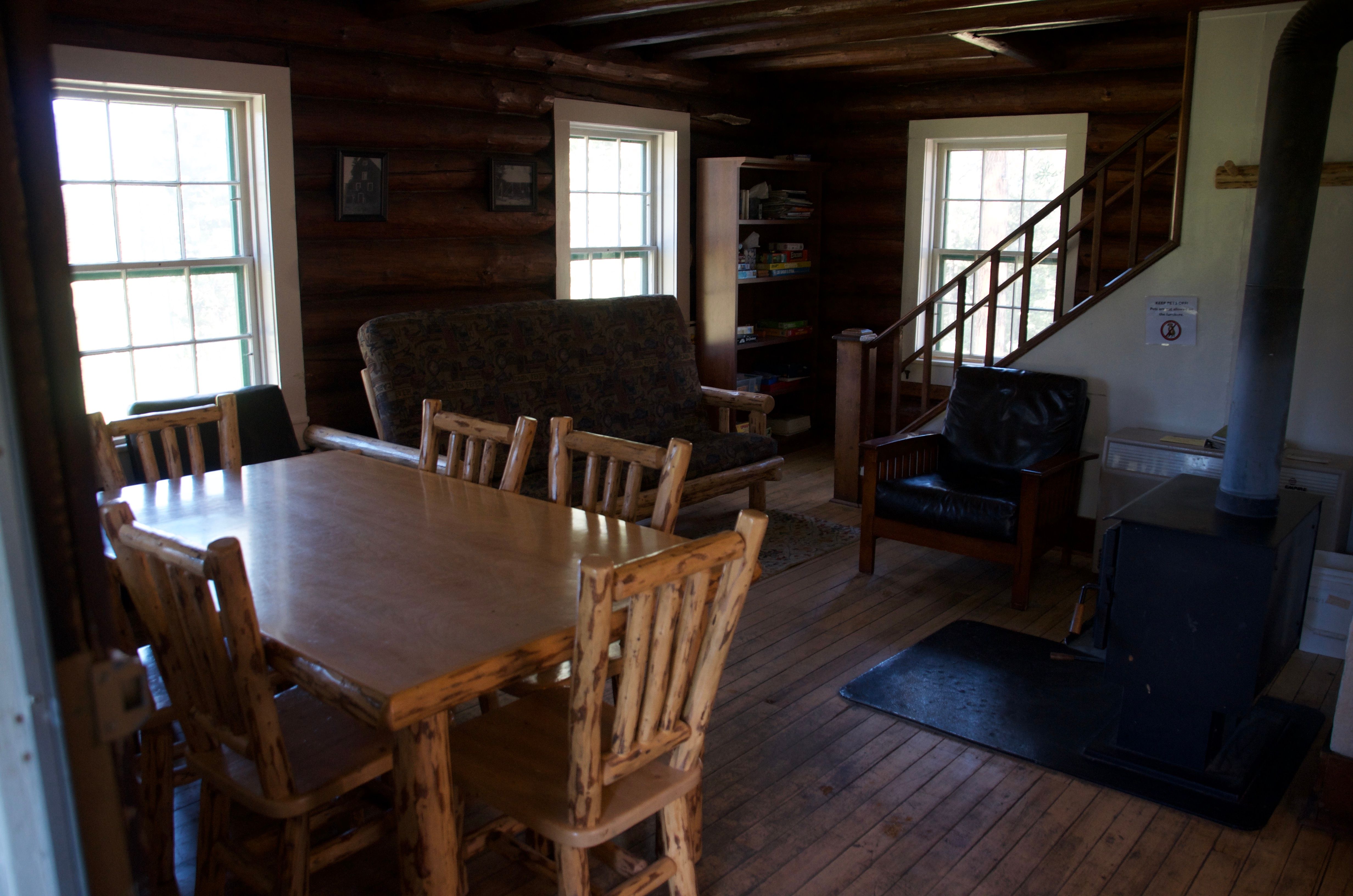 The Old Condon Ranger Station main floor with log dining table, futon couch, bookshelf, wood stove, and original log walls