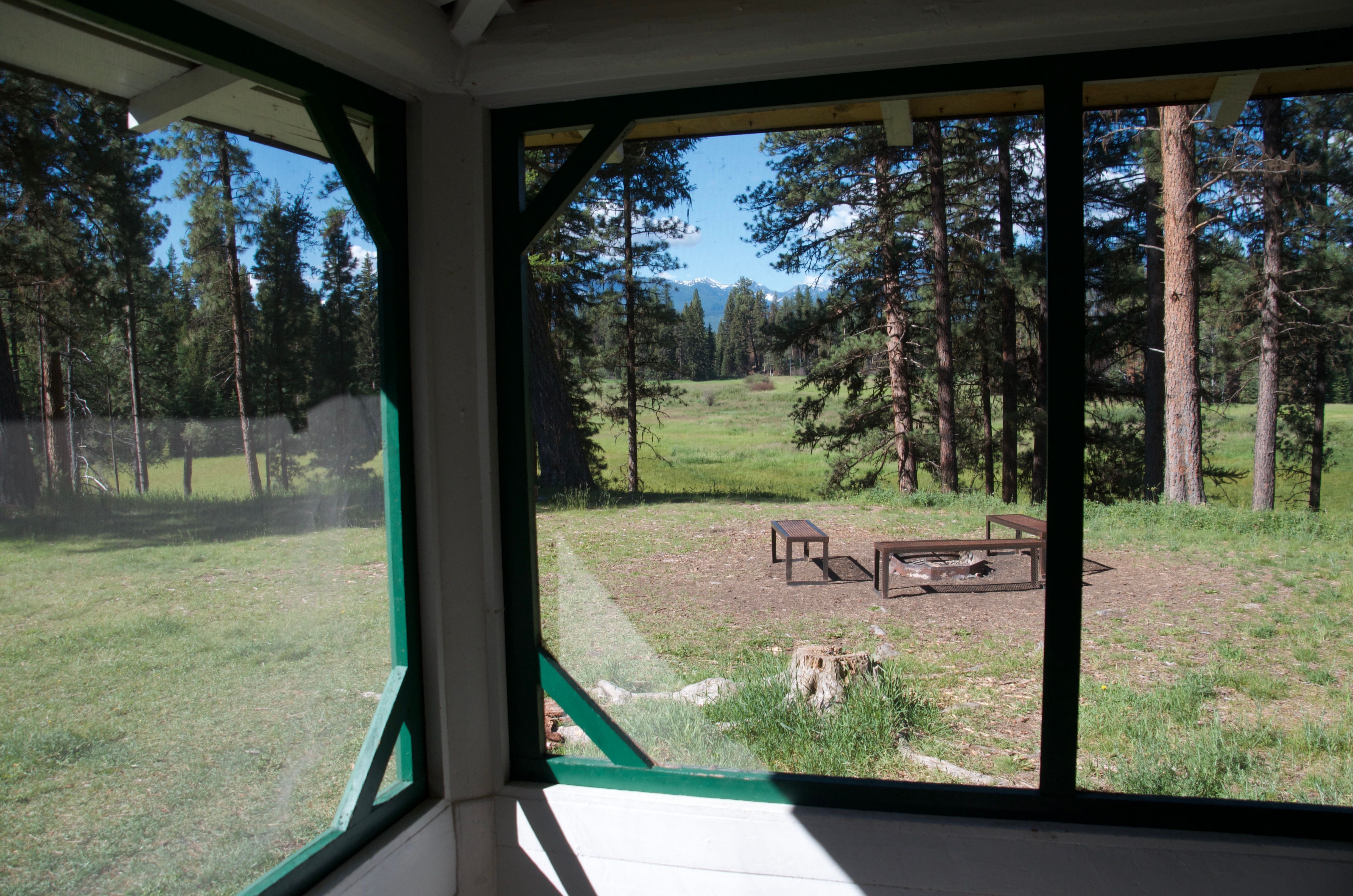View from the screened front porch of the Old Condon Ranger Station looking out at the fire pit, open meadow, and distant mountains