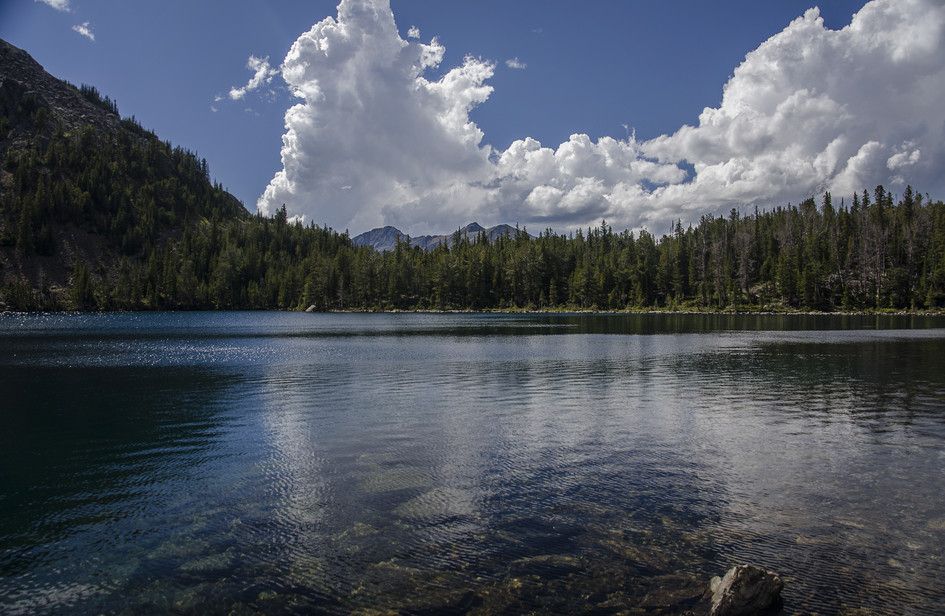 Louise Lake reflecting dramatic clouds with forested shore and distant peaks