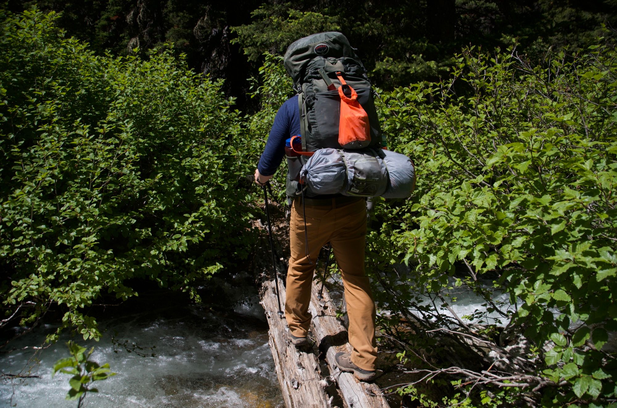 Backpacker balancing across log over rushing creek
